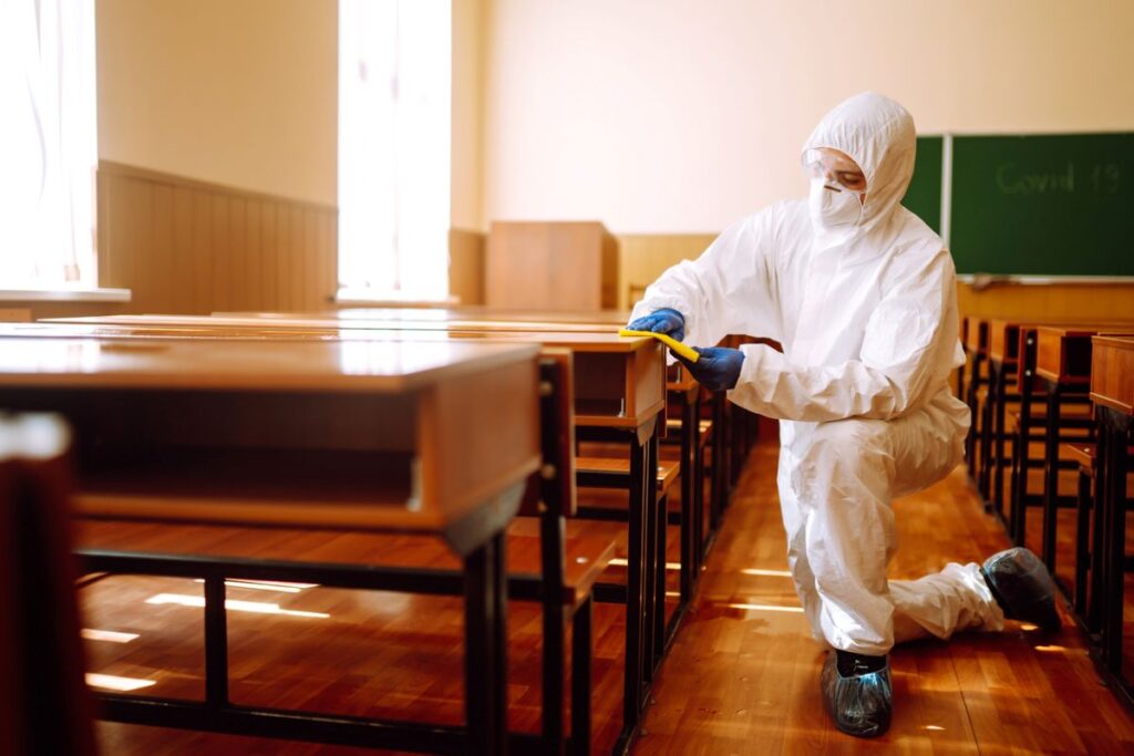 Pest control technicians wash desks inside of a classroom.