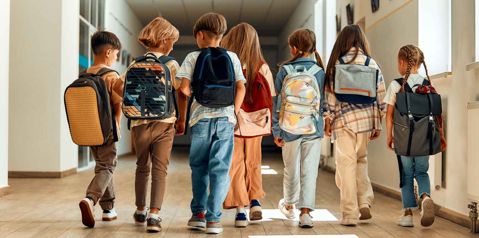 School children walking down the hallway with backpacks on.