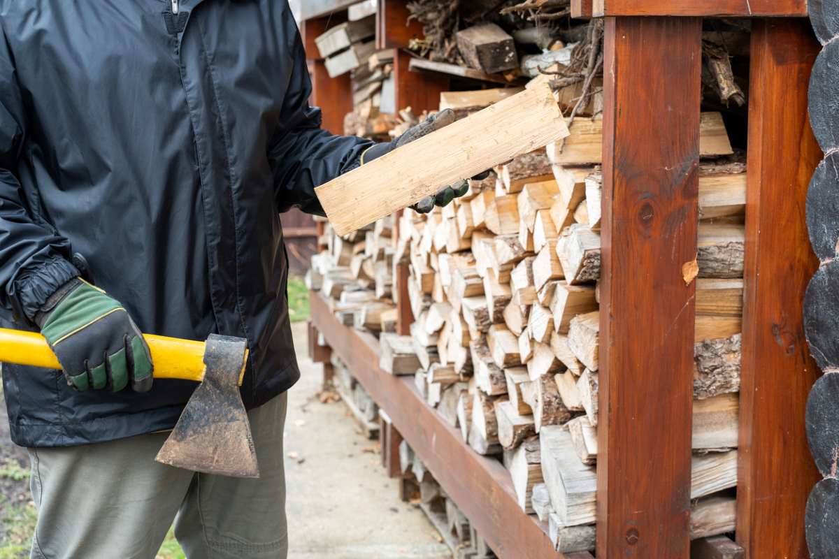 A person wielding an ax storing firewood on a designated rack.