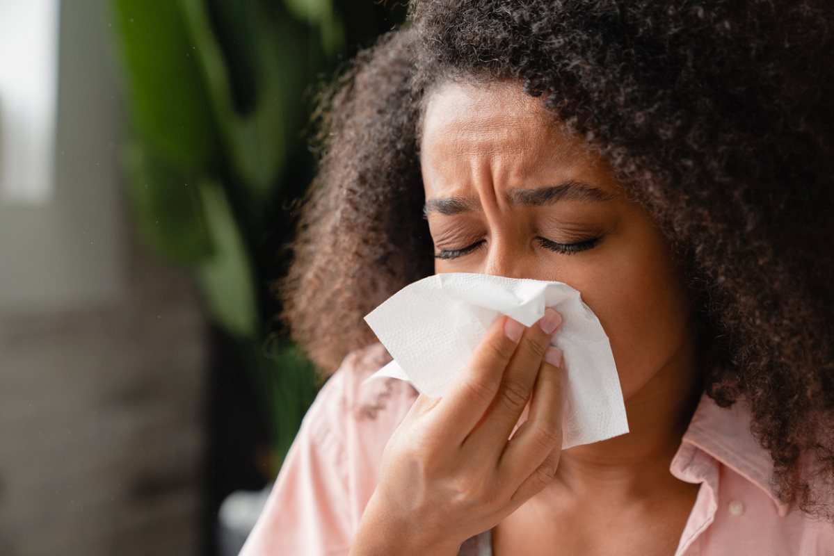 A young woman with allergies blowing her nose into a tissue. 