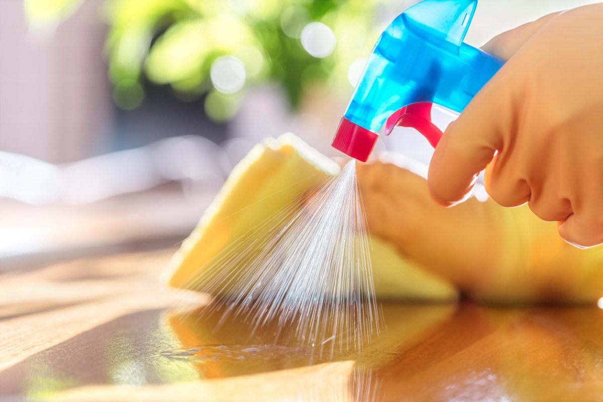 A person cleans a countertop with a spray, cloth, and rubber gloves post-fumigation.