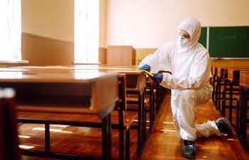 Pest control technicians wash desks inside of a classroom.