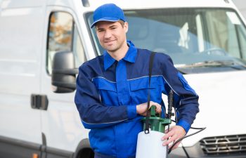 Pest control technician carrying pesticide with truck parked in the background.